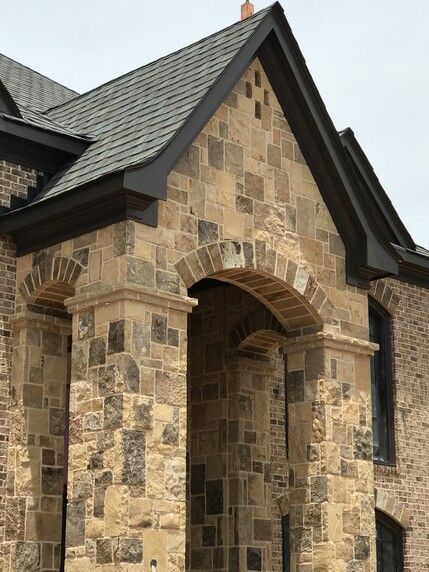Stone facade with arched entryway under a roof, dark trim, and windows.