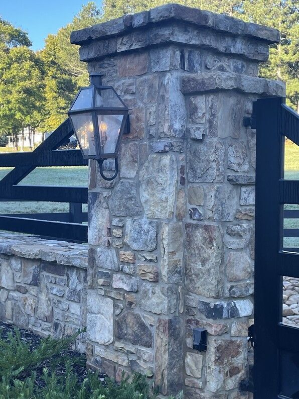 Stone pillar with lantern and black gate in a grassy setting.