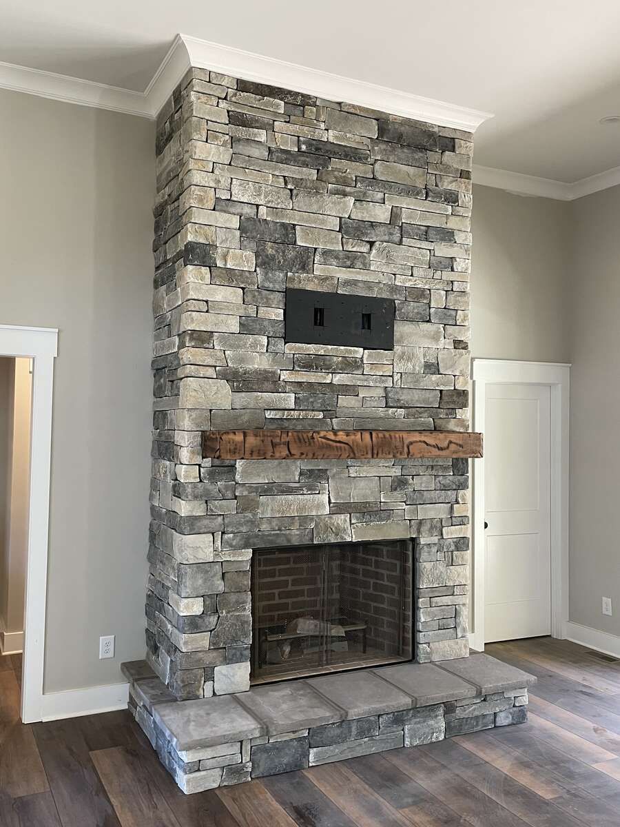 Stone fireplace with a wooden mantle and built-in screen, in a room with light-colored walls and wood flooring.