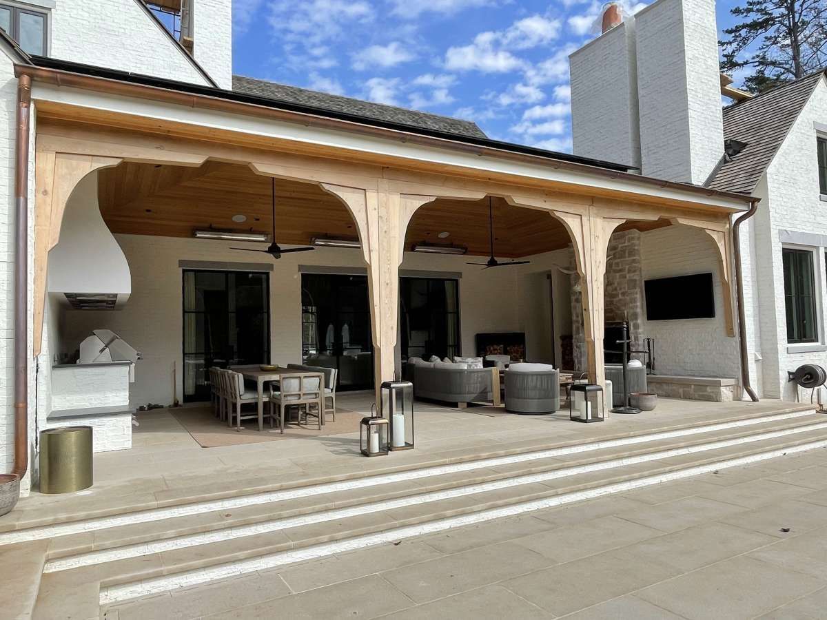 Covered outdoor patio with seating, fireplace, and television. Beige stone and wood construction.