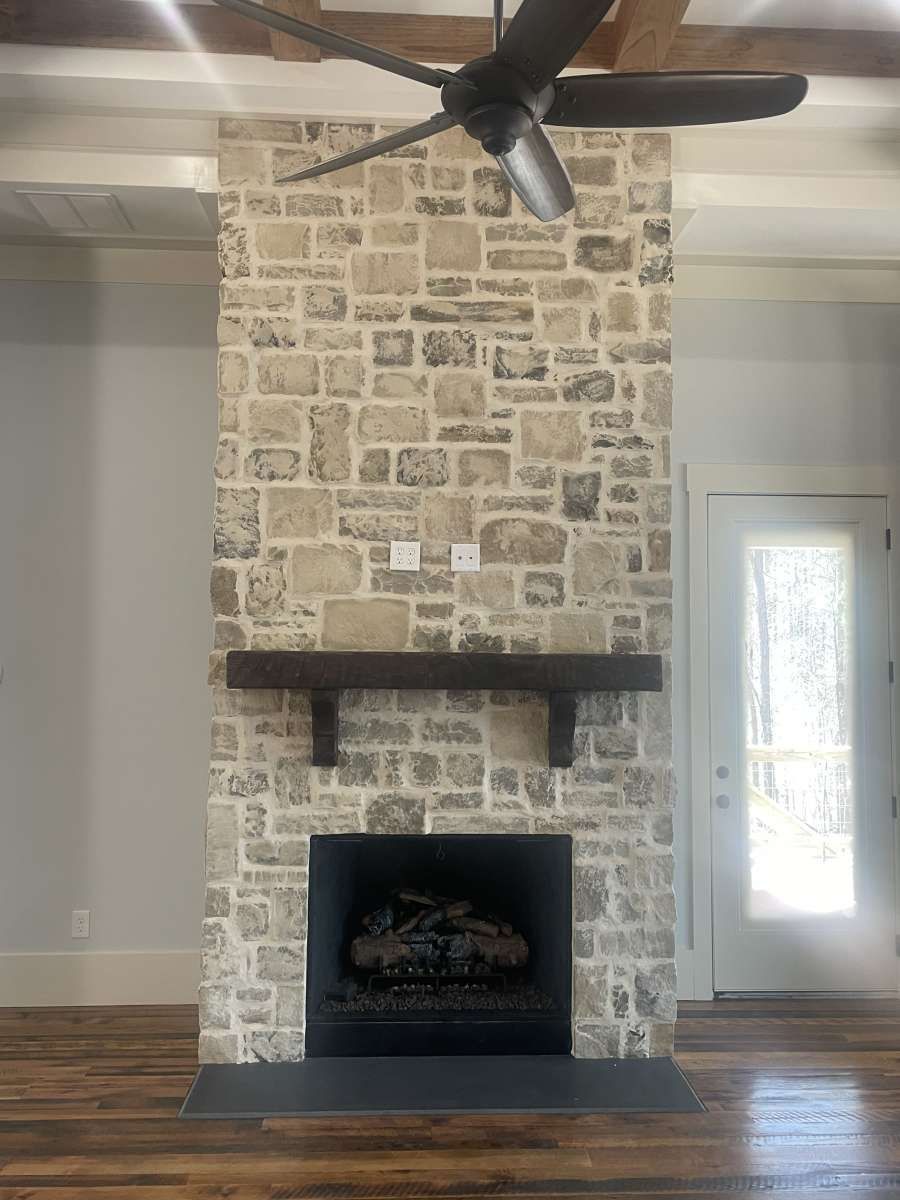 Stone fireplace with dark wood mantel, black firebox, and a ceiling fan.