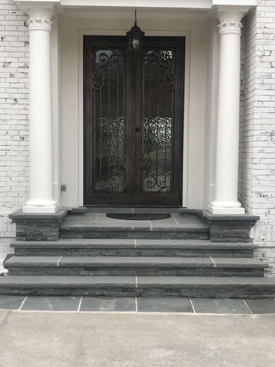 Two dark doors with ironwork, between white columns, on stone steps.