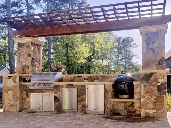 Outdoor kitchen with grill, smoker, and cabinets, under a wooden pergola.
