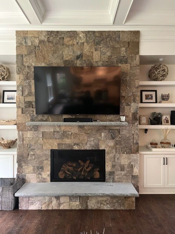 Stone fireplace with built-in TV and shelves. Dark wood floor, white cabinets, neutral tones.