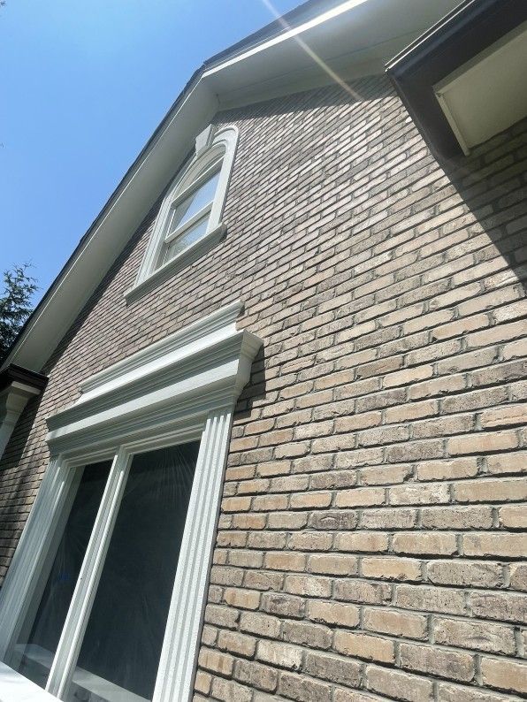 Brick exterior of a house with white trim around windows and eaves under a bright blue sky.