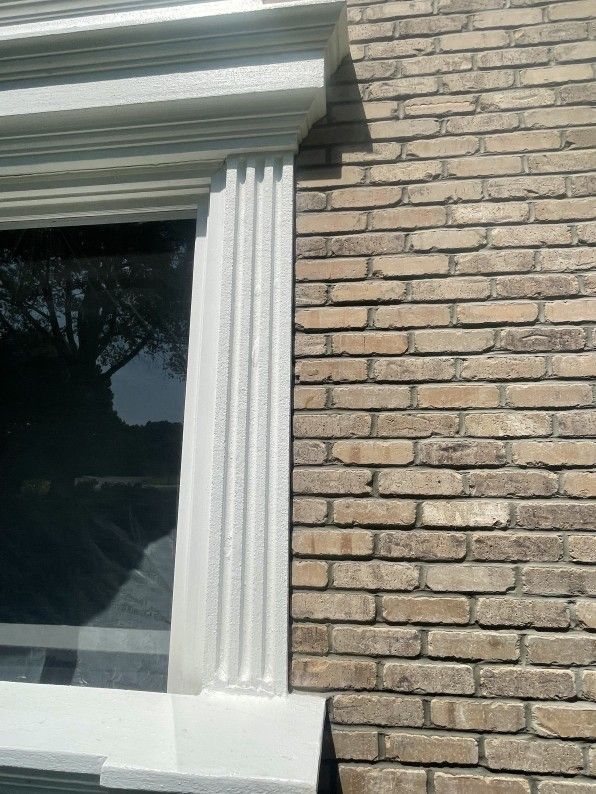 White window frame with fluted column detail next to a brick wall.