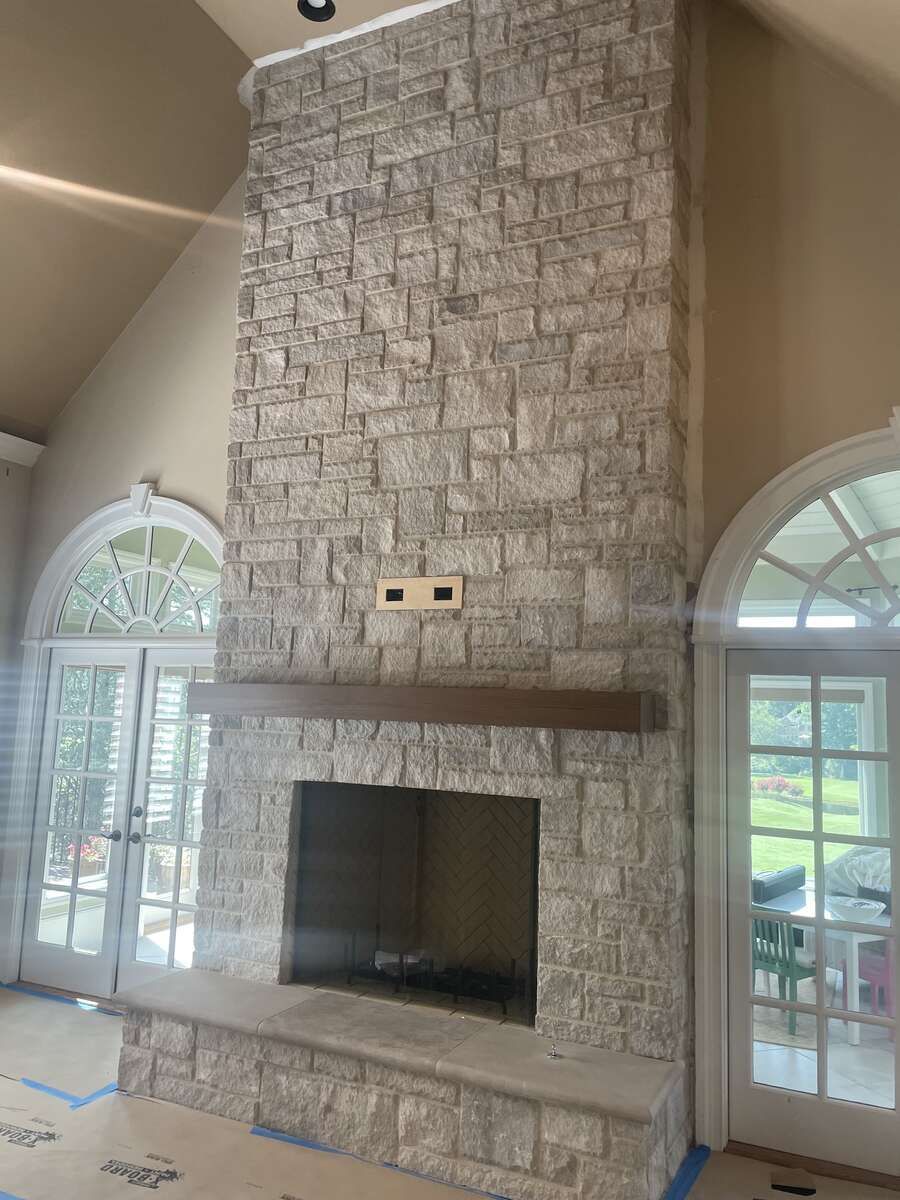Stone-covered fireplace with a wooden mantle and light-colored stone surround; flanked by arched windows and doors.