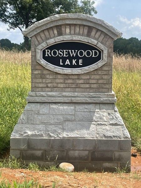 Rosewood Lake sign made of brick and stone in a field. Black oval with white text.