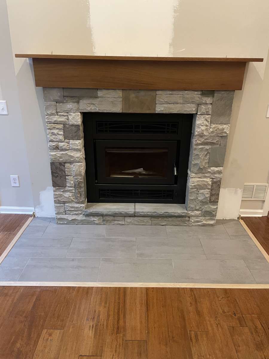 Fireplace with stone surround and wooden mantel; gray tile hearth; wood flooring.