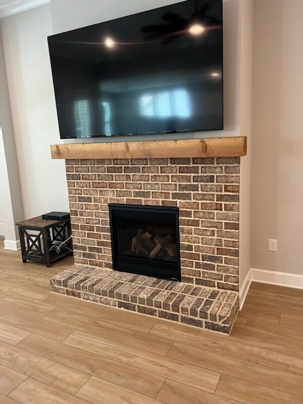 Fireplace with brown brick, black fireplace insert, wooden mantel, and TV.