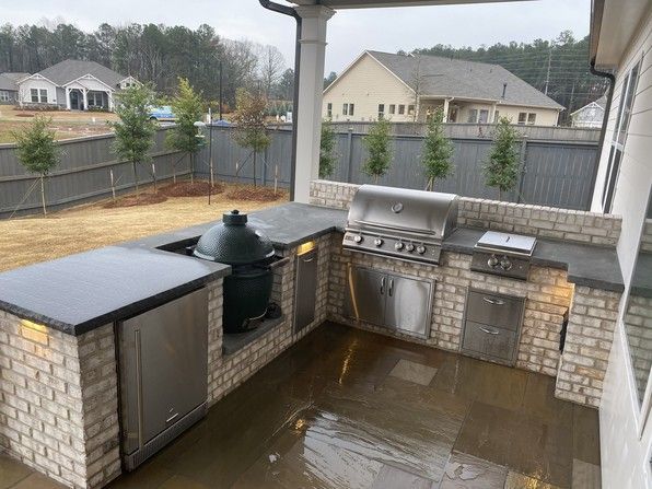Outdoor kitchen with brickwork, stainless steel appliances, and Big Green Egg grill.