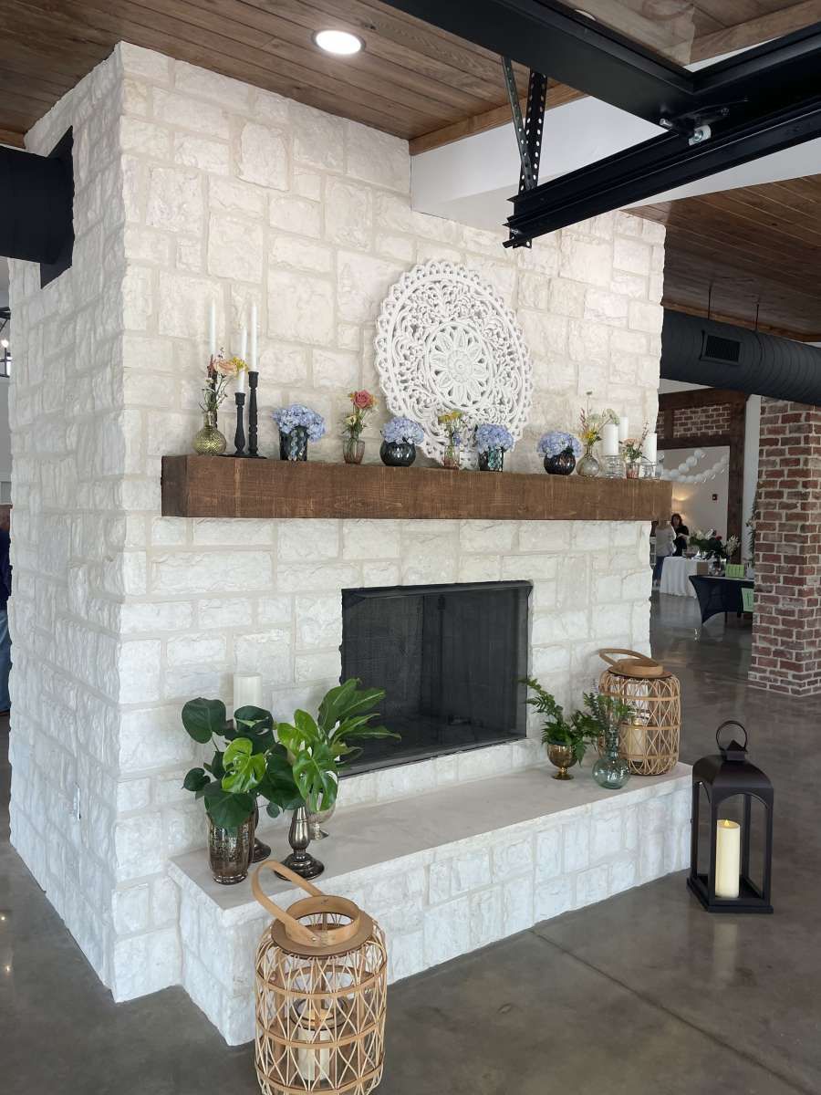 White stone fireplace with a wooden mantel, decorated with flowers and candles.