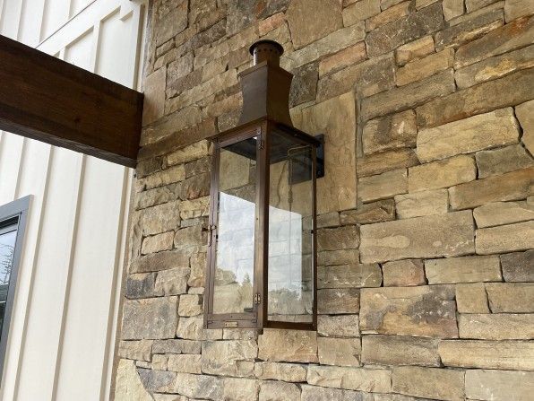 Bronze lantern on stone wall, next to a wooden beam.