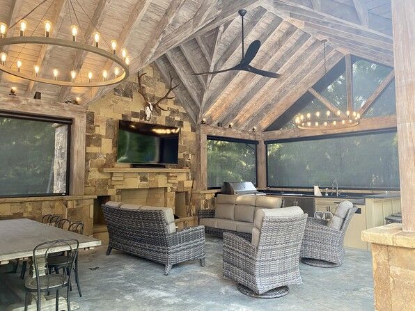 Outdoor patio with stone fireplace, seating, and a large TV under a wood ceiling.