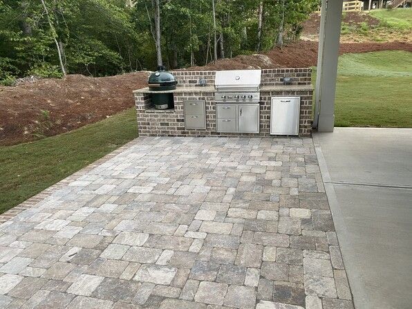 Outdoor kitchen on a paved patio with a grill, Big Green Egg, and refrigerator.