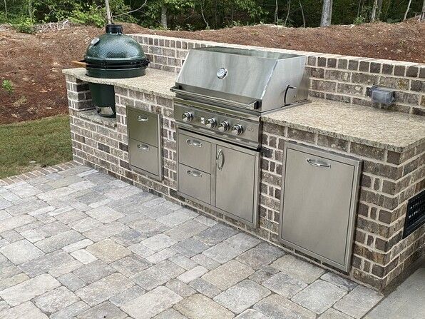 Outdoor brick kitchen with grill, Big Green Egg, granite countertop, and stainless steel cabinets.