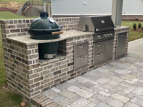 Outdoor kitchen with brick and stone, includes a grill, Big Green Egg, and storage cabinets.