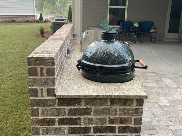 Green ceramic grill on a brick and granite outdoor countertop.