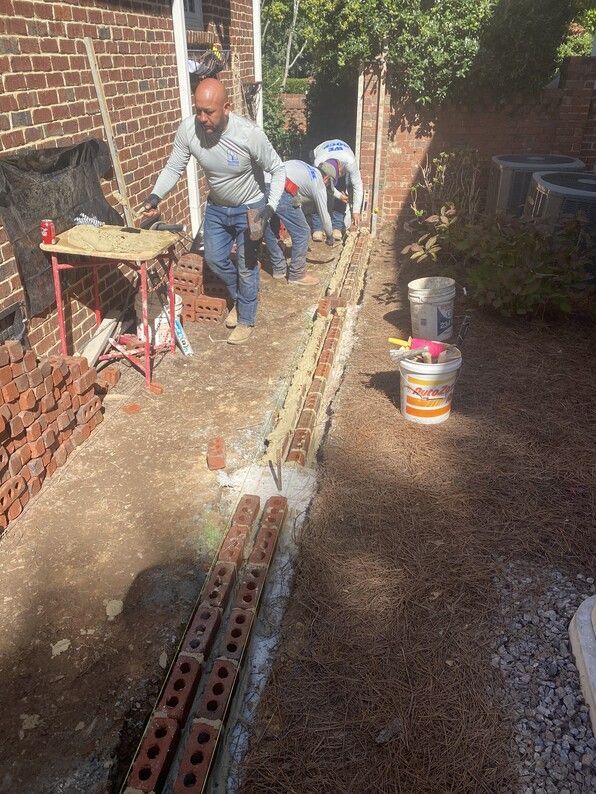 Bricklayers building a low wall. Workers lay bricks in mortar along a narrow trench.