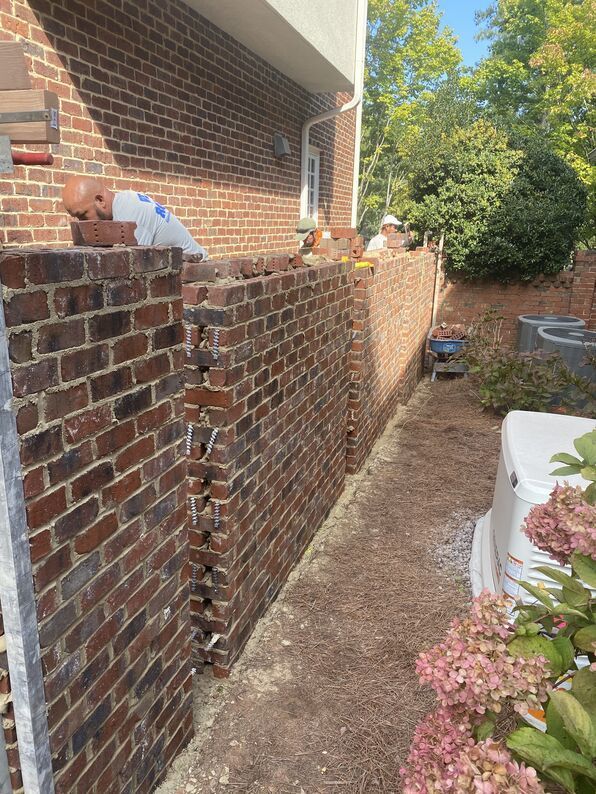 Brick retaining wall under construction next to a house; workers visible.