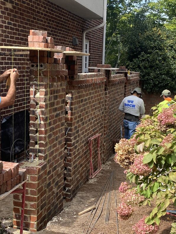 Bricklayers constructing a brick wall next to a building, using a level guide.
