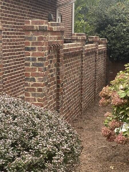 Brick wall with decorative pillars, brown mulch, and green shrubs.