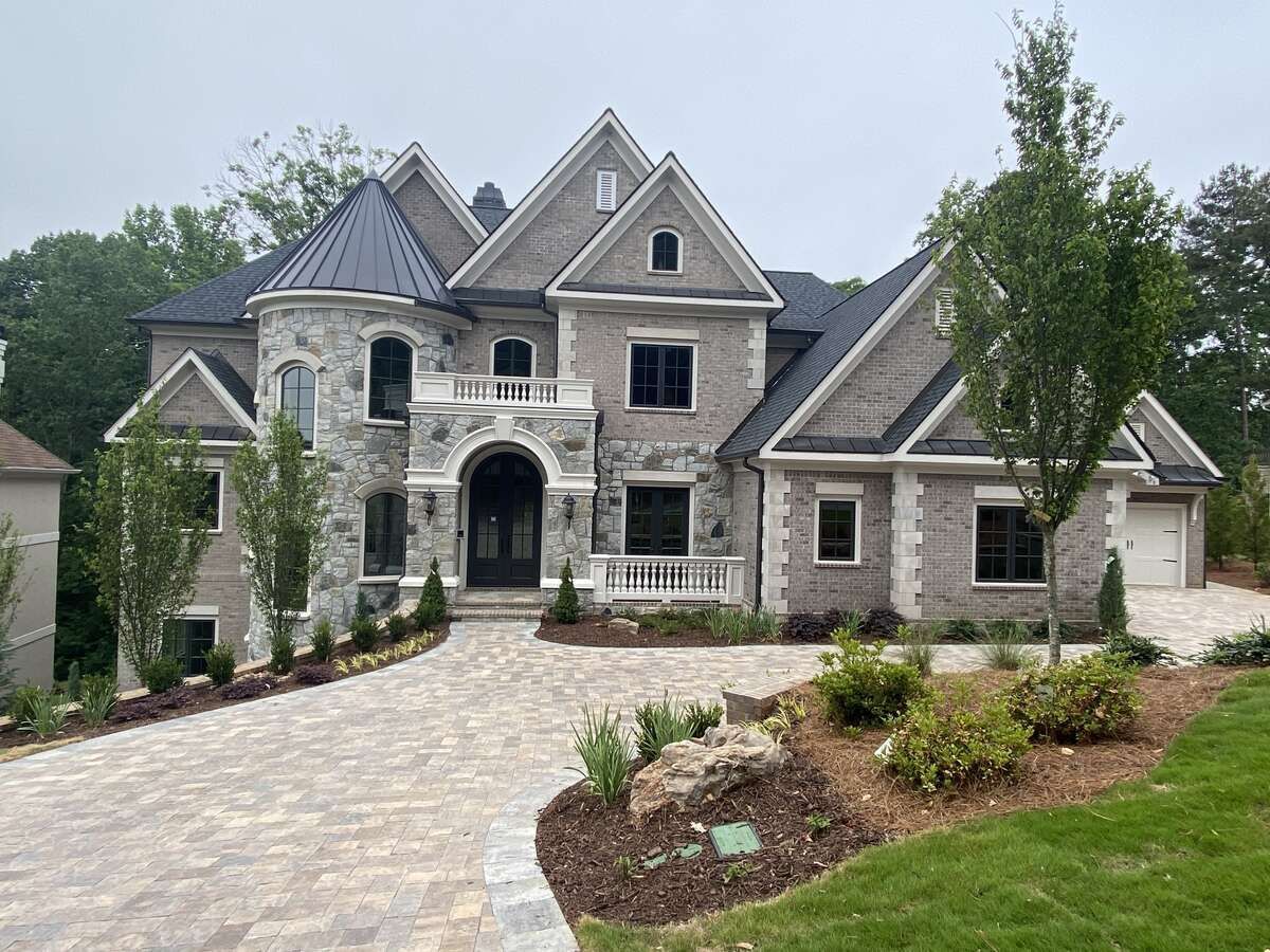 Two-story house with stone facade, arched entry, brick accents, and a paved driveway.