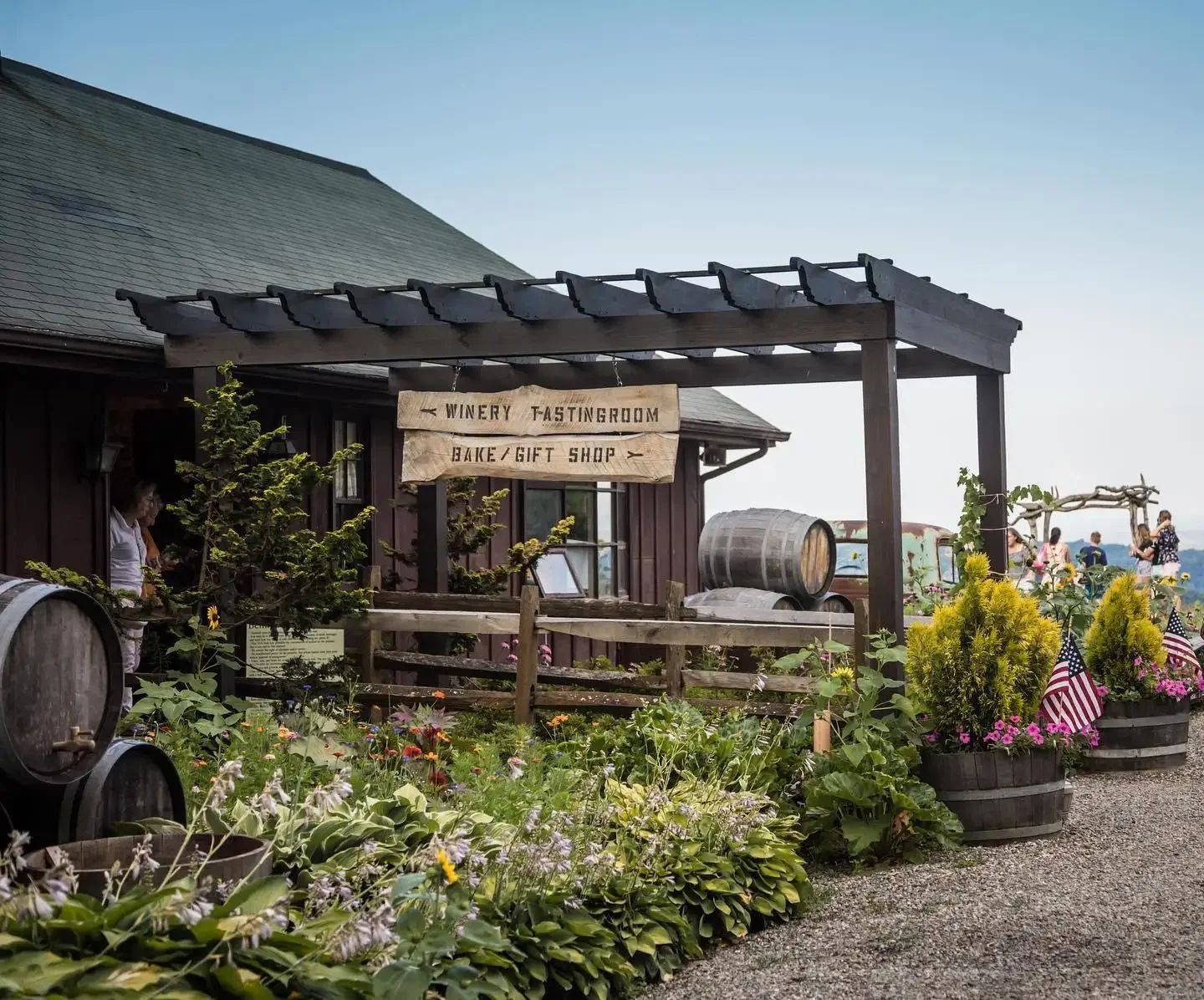 A house with a pergola and barrels in front of it.