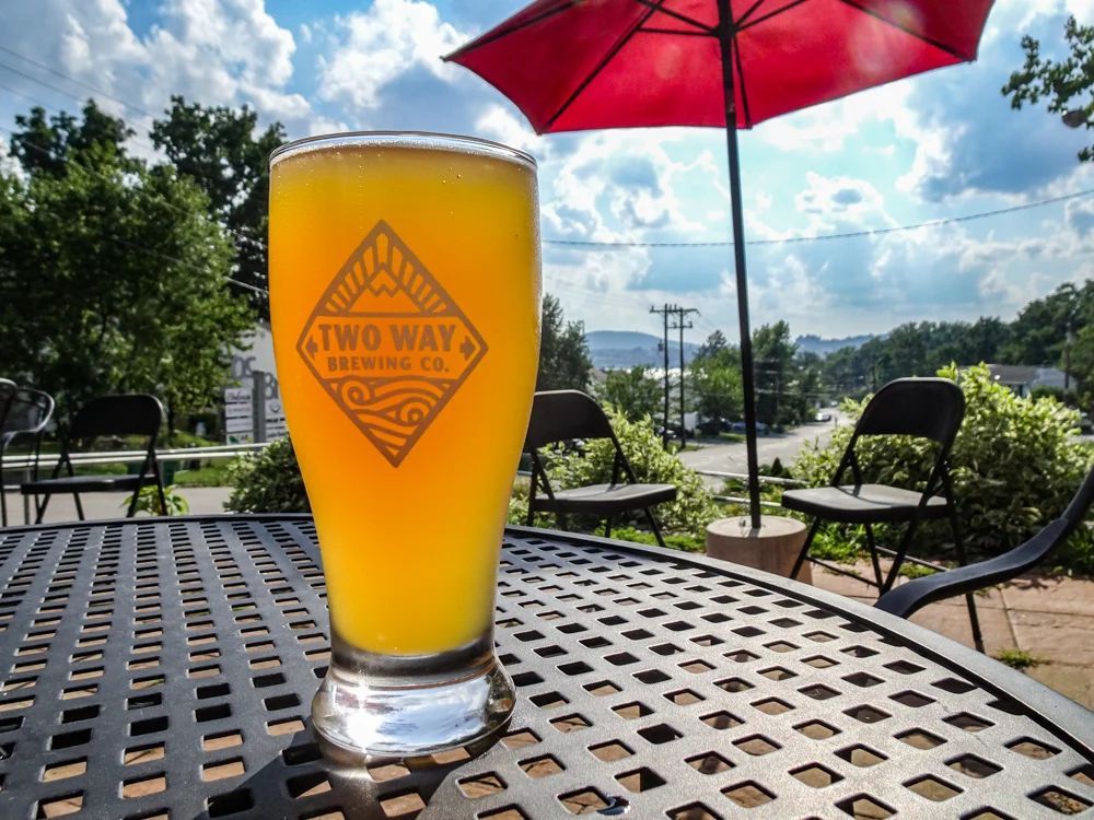 A glass of beer is sitting on a metal table under an umbrella.