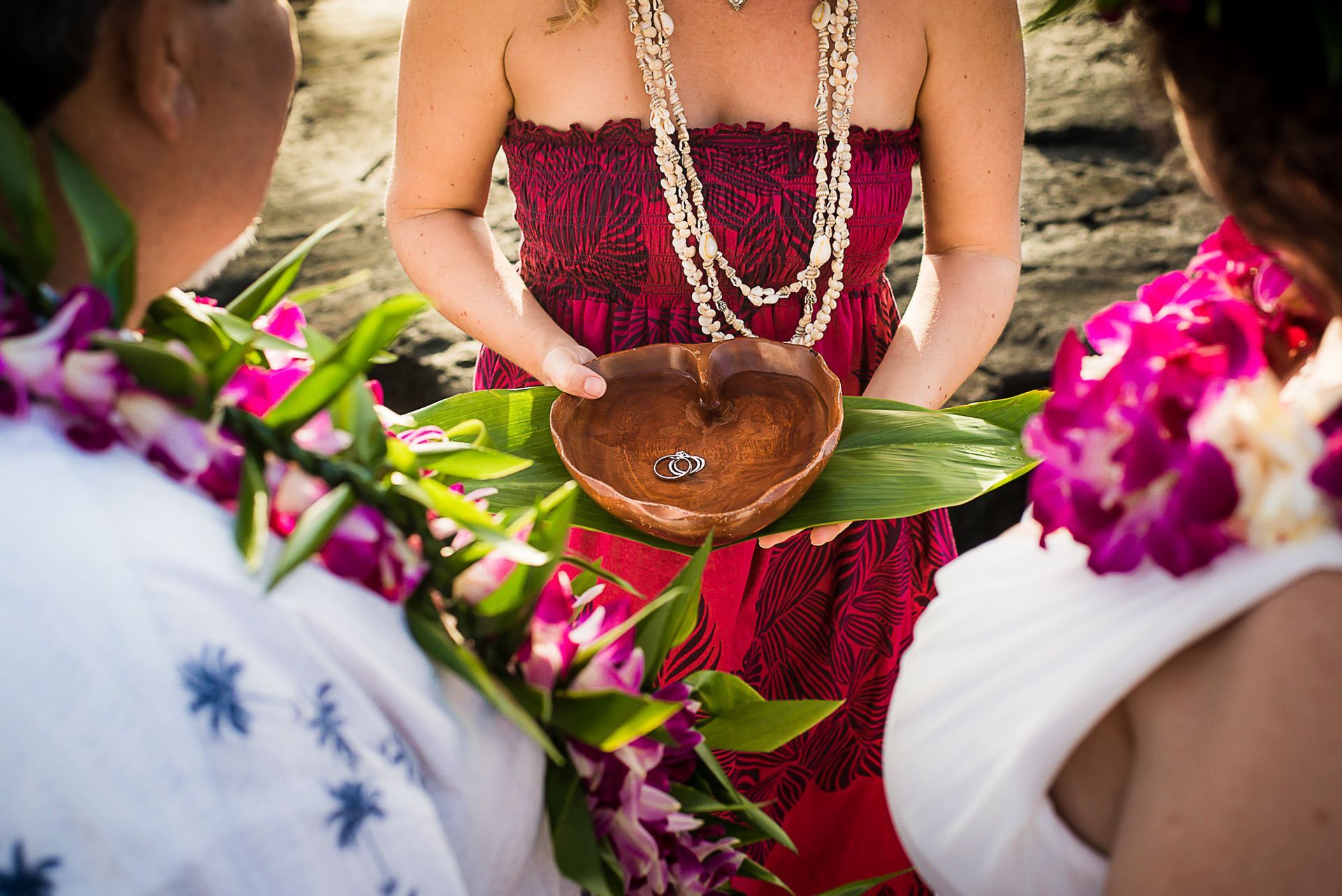 Woman in a red dress holding a coconut bowl during a flower-filled ceremony