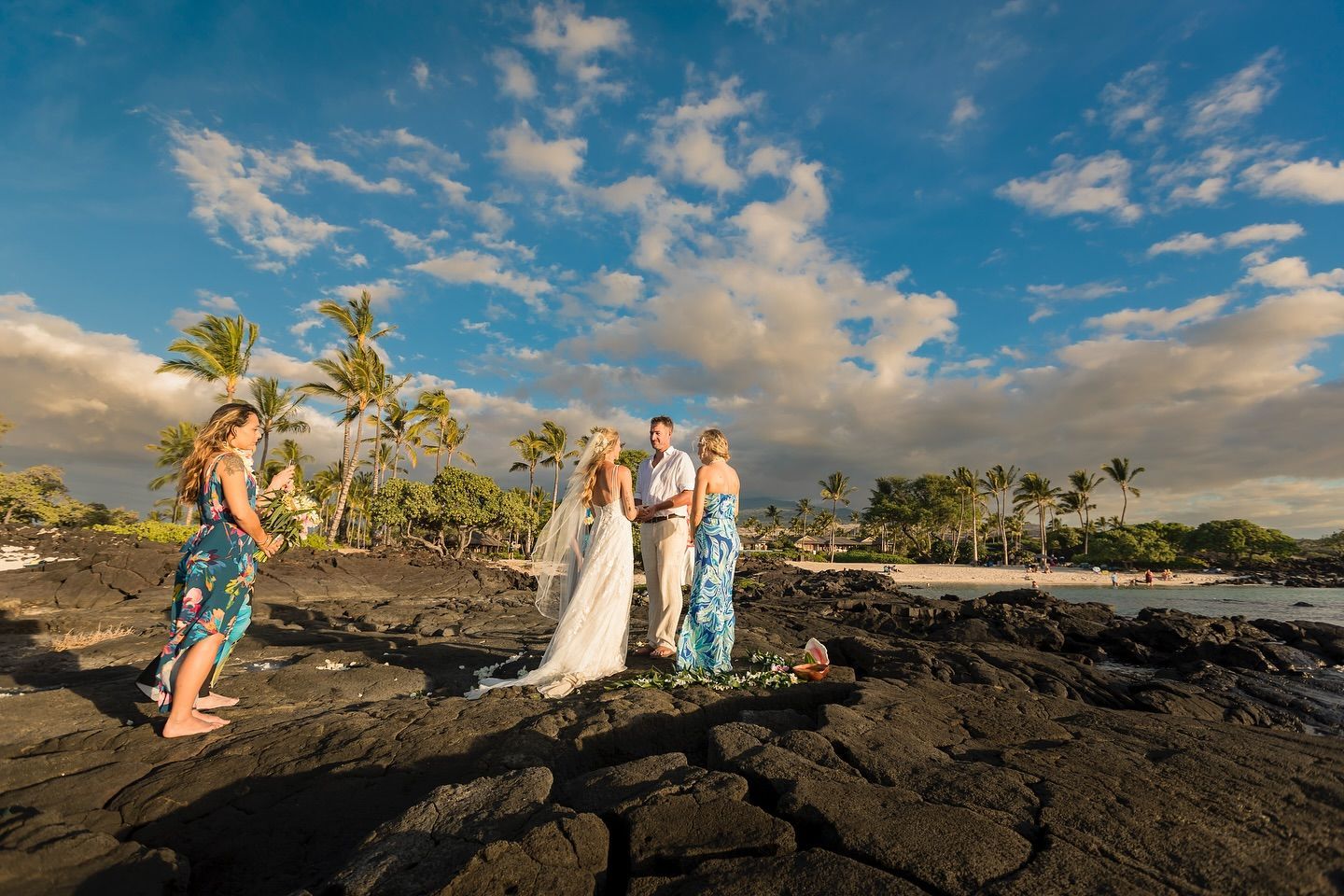 Wedding couple and guests posing on black lava rocks by the ocean under a cloudy sky