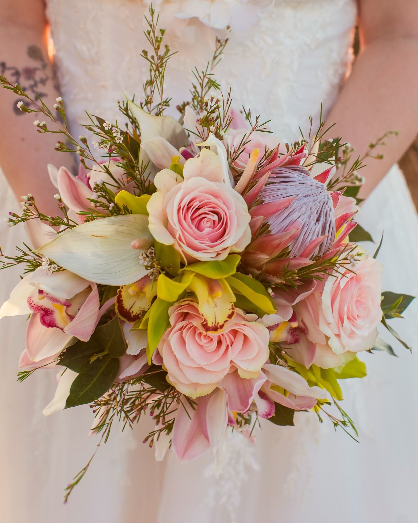 Pastel pink bridal bouquet with roses, lilies, and greenery held against a white wedding dress