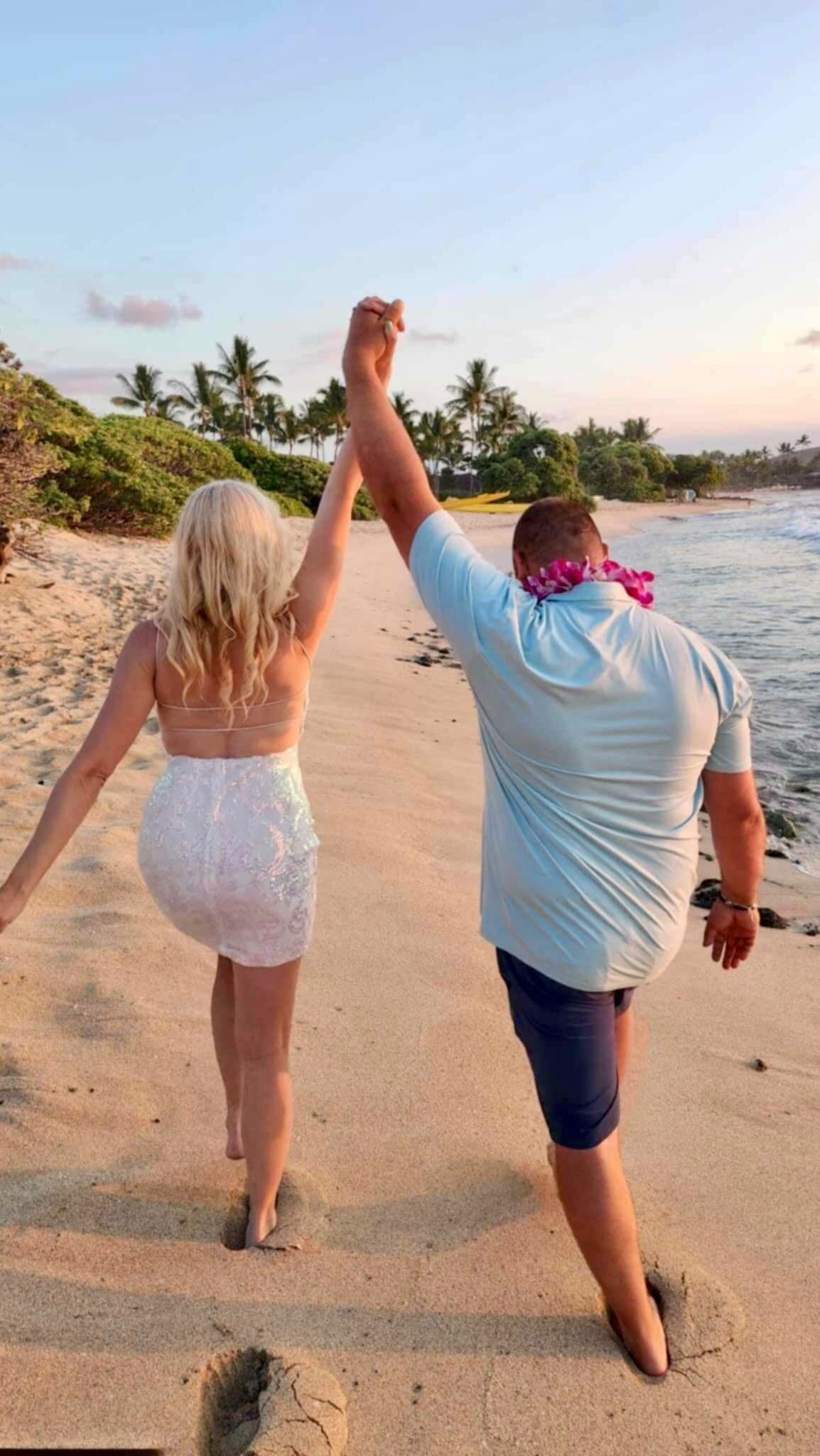 Two people holding hands and walking along a sandy beach at sunset.