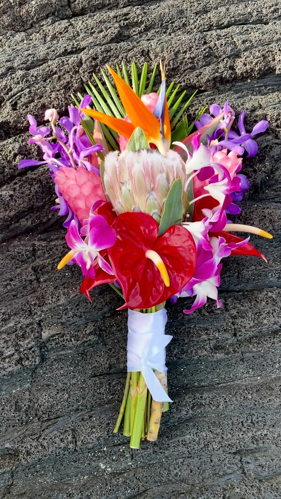 Colorful tropical flower bouquet with pink, purple, red, and orange blooms against a rock background