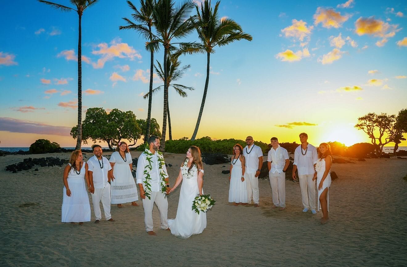 Wedding party in white at sunset on a beach with palm trees and a bride holding a bouquet