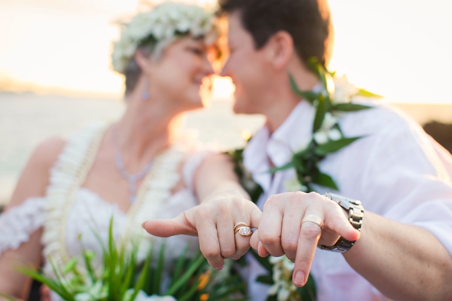 Couple at sunset wedding, showing off rings. Bride wearing flower crown.