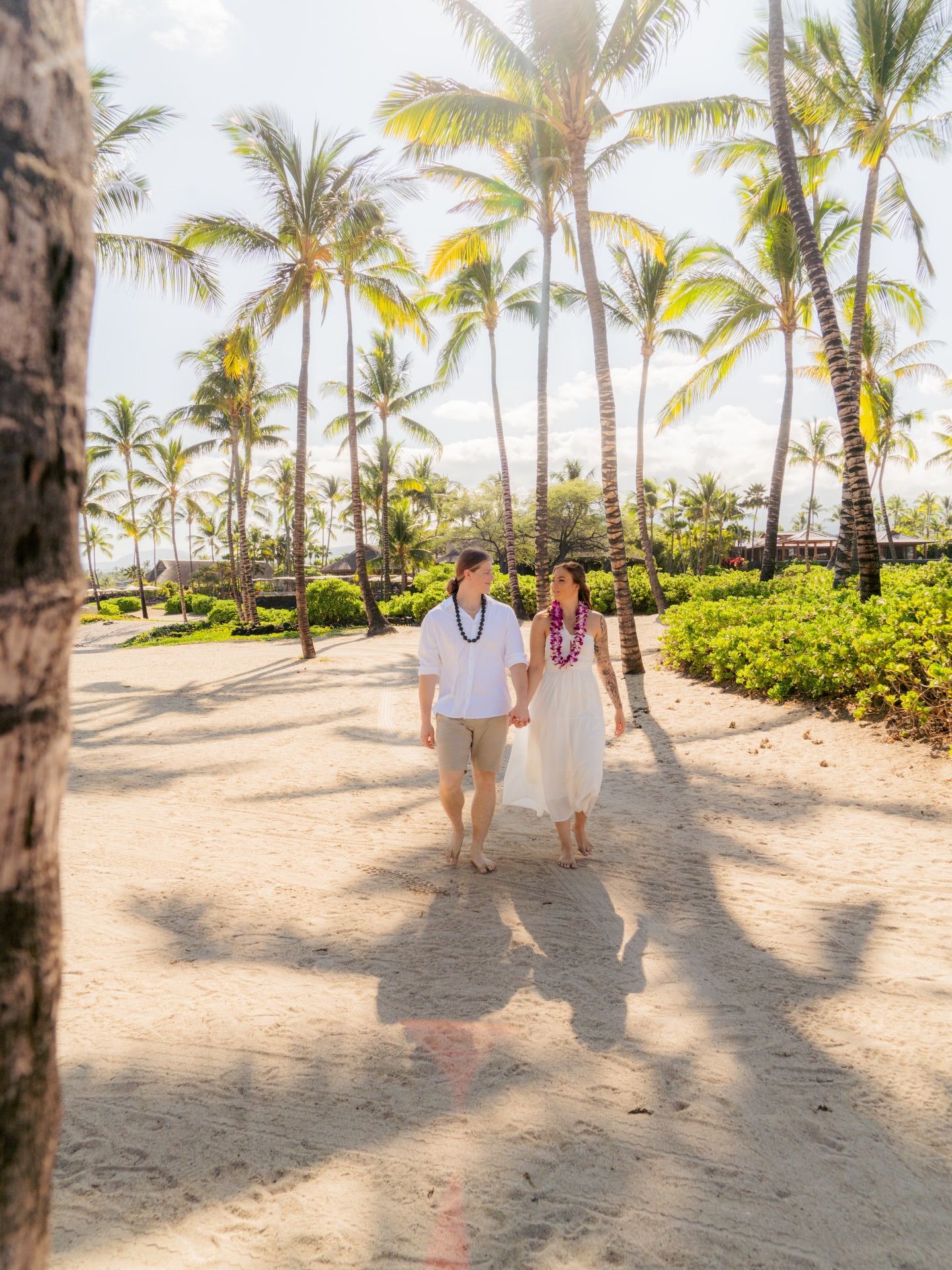 Two people walking on a sunny palm-lined path near a beach