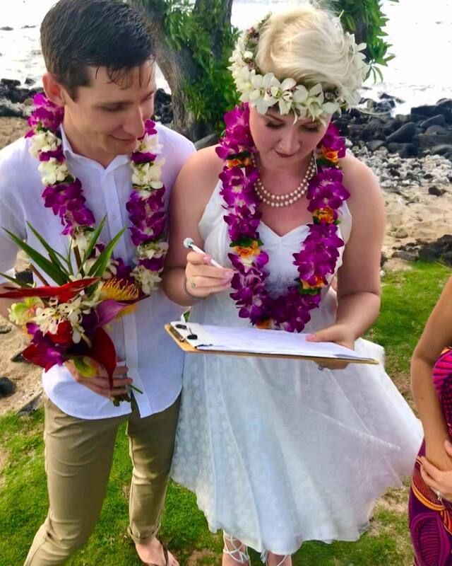 Two people in white leis with a clipboard outdoors by the water at a beach wedding ceremony by Simple Kona Beach Weddings.