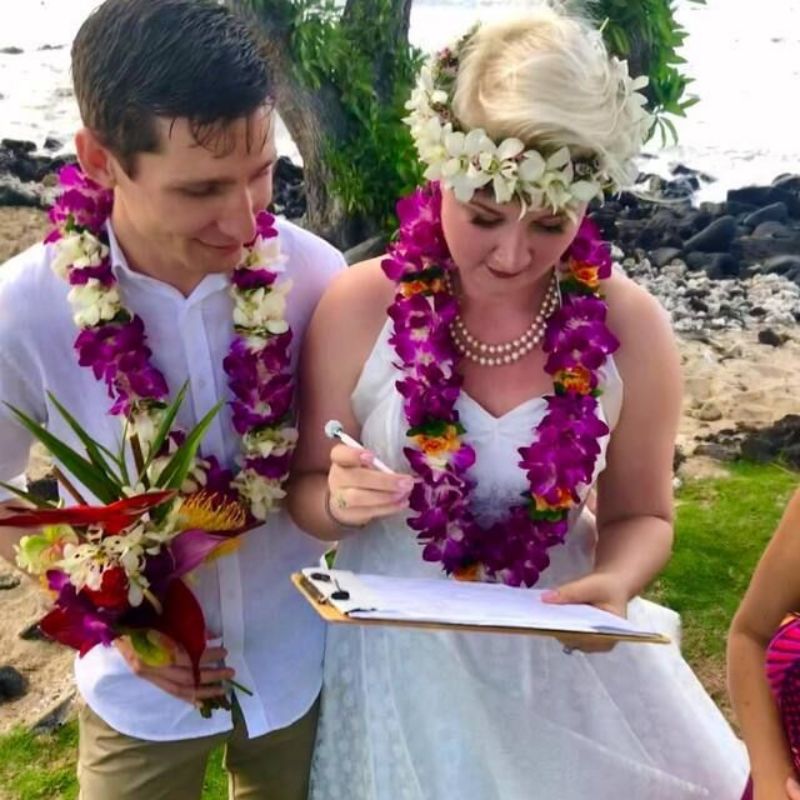 Couple holding hands at outdoor wedding ceremony on rocks near water.