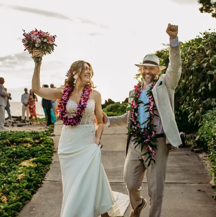 Photograph of a newlywed couple celebrating outdoors on a pathway surrounded by greenery.