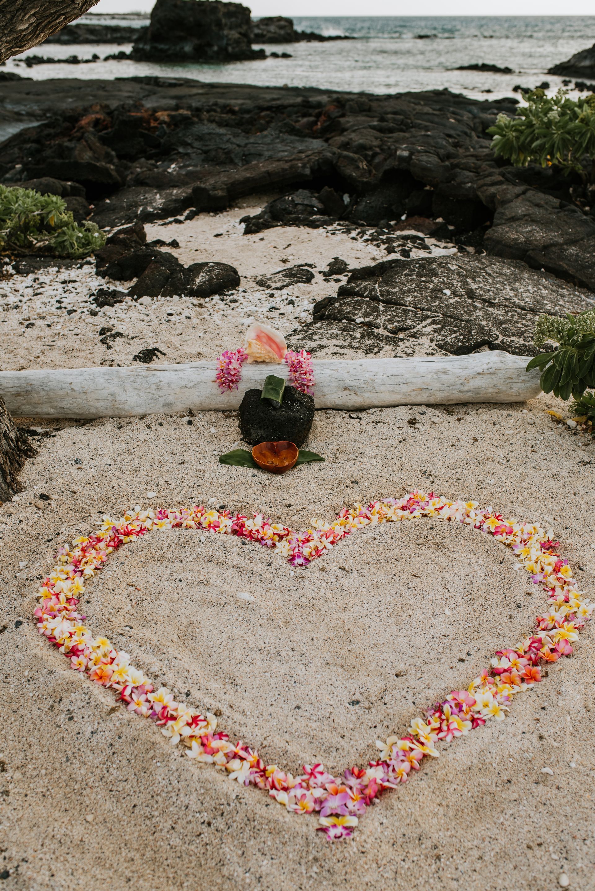 Couple holding hands at outdoor wedding ceremony on rocks near water.