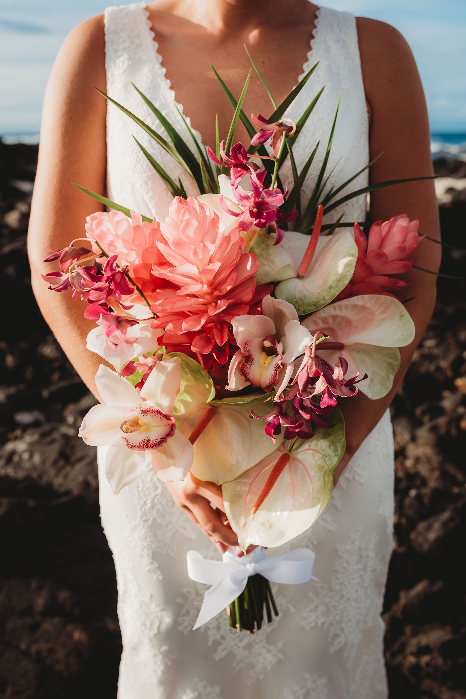 Bride holding a pink and white tropical bouquet by Simple Kona Beach Weddings in a white dress on a beach