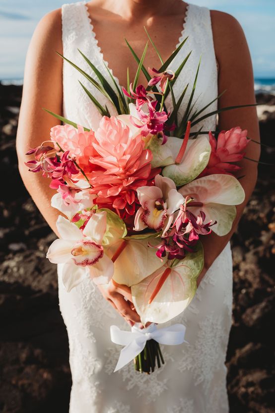 Bride holding a pink and white tropical bouquet in a white dress on a beach