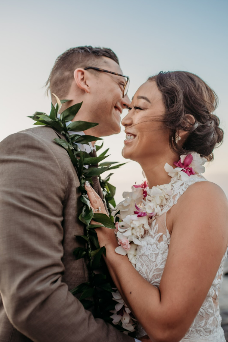 Simple Kona Beach Weddings couple embracing and laughing. Couple wearing leis. Groom wearing a tan suit, bride in white.