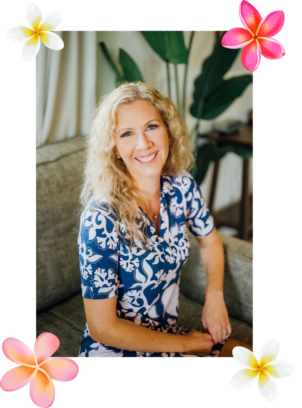 Smiling woman in a blue floral dress seated indoors, framed by pink and white flowers.