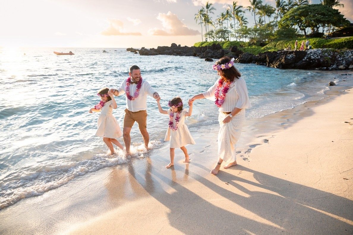 A vow renewal couple walks along a beach in Kailua-Kona, HI, with their children after renewing thei