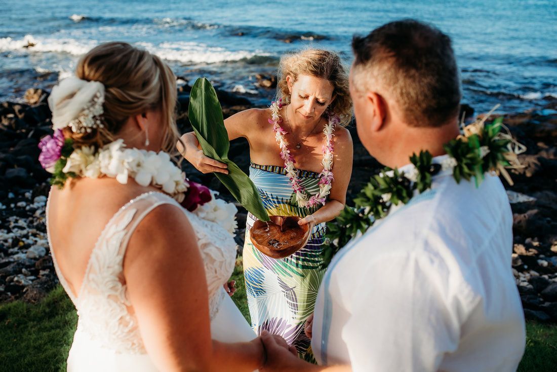 Wedding ceremony on the beach, officiant with couple, leis, ocean background.