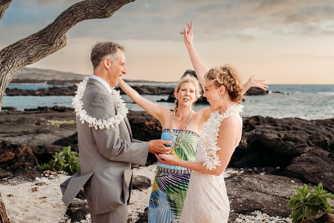 Wedding on beach: groom holds bride's hand, woman raises arms in celebration, ocean in background.