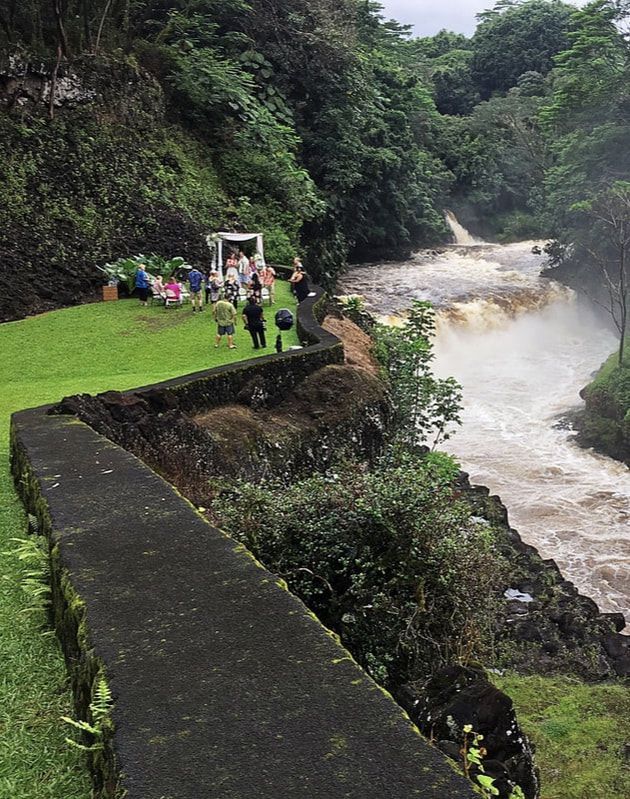 People near a white waterfall in a lush green riverside gorge, viewed from a stone path