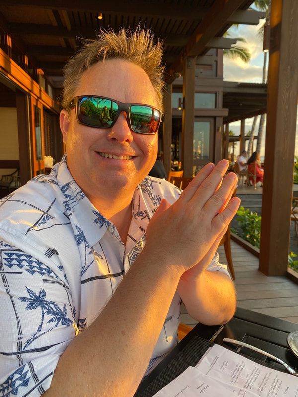 Man in sunglasses, clapping hands at an outdoor restaurant. Palms reflecting green and the golden light of sunset.